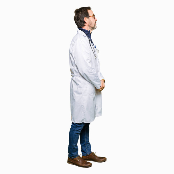 Handsome middle age doctor man wearing medical coat looking to side, relax profile pose with natural face with confident smile. - Zdjęcie, obraz