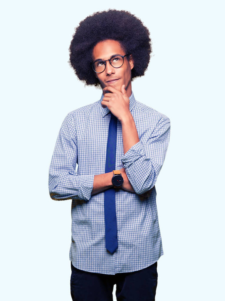 Giovane uomo d'affari afro-americano con i capelli afro che indossa occhiali con la mano sul mento pensando alla domanda, espressione pensierosa. Sorridente con la faccia pensierosa. Concetto di dubbio
. - Foto, immagini