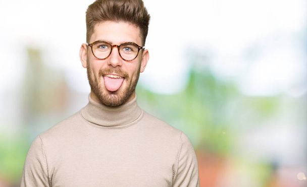 Mladý pohledný obchodní muž nosí brýle držet jazyk ven spokojený s legrační výraz. Koncept emoce. - Fotografie, Obrázek