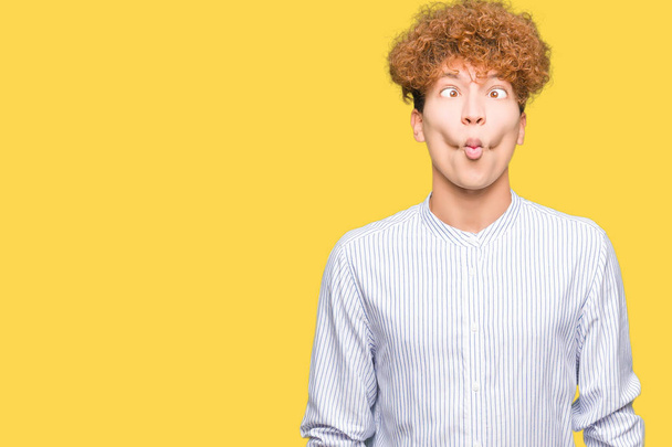 Young handsome business man with afro hair wearing elegant shirt making fish face with lips, crazy and comical gesture. Funny expression. - Photo, Image