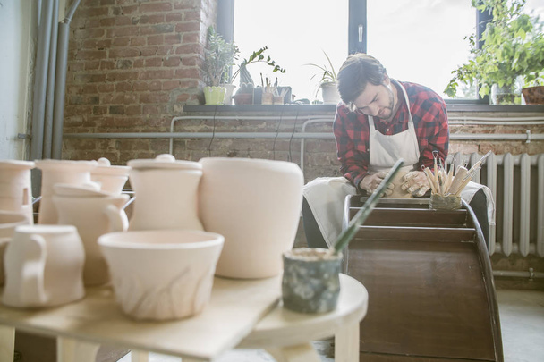 Jeune potier prospère en vêtements de travail travaillant sur un nouvel objet en argile dans son propre atelier
 - Photo, image