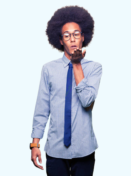 Young african american business man with afro hair wearing glasses looking at the camera blowing a kiss with hand on air being lovely and sexy. Love expression. - Foto, Imagen