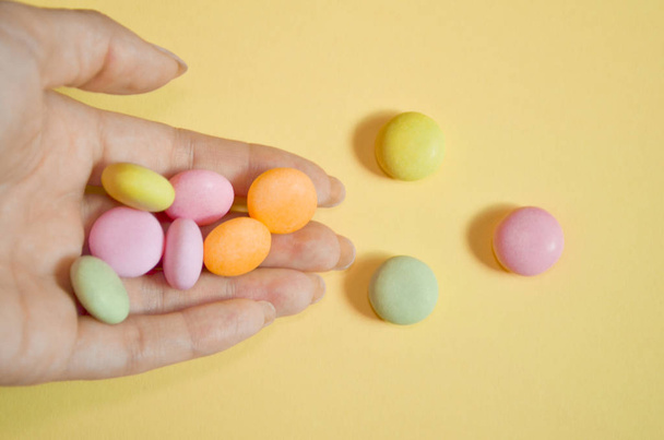 Round colored candies lie in a bunch on hand on yellow color, with copyspace, closeup - Photo, Image