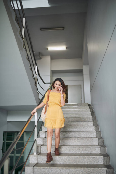 glückliche junge Frau geht die Treppe hinunter, telefoniert mit dem Handy - Foto, Bild