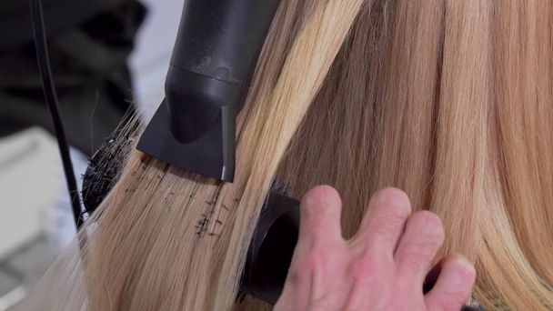 Ковзаючий знімок професійного перукаря, який висушує волосся свого клієнта
 - Фото, зображення