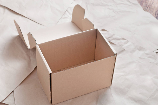 Brown carton box laying on sheets of crumpled kraft paper. - Foto, afbeelding