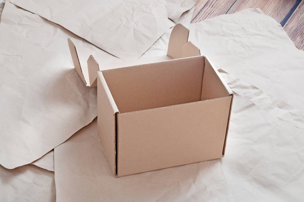Brown carton box laying on sheets of crumpled kraft paper. - Fotografie, Obrázek