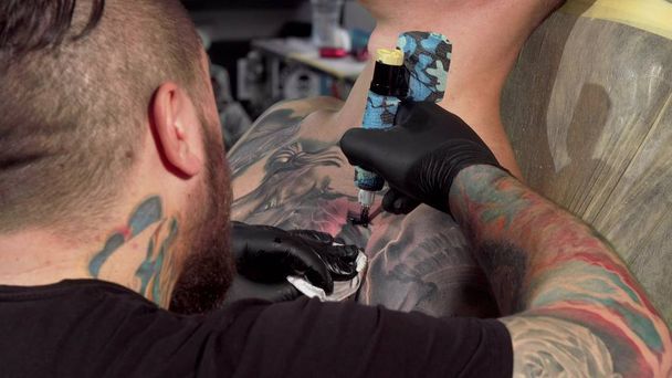 Vista trasera de un artista del tatuaje haciendo un tatuaje en el pecho de un cliente masculino
 - Foto, Imagen