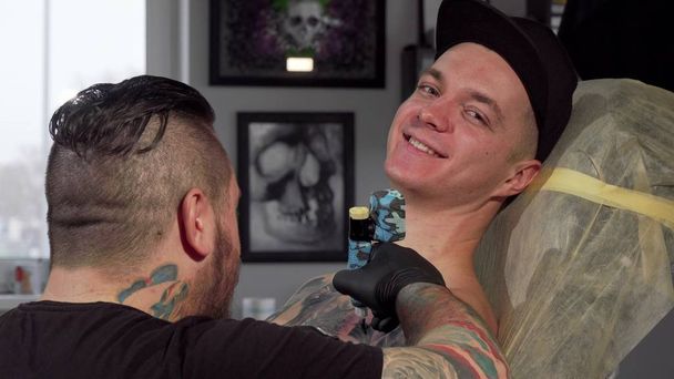 Cheerful young man smiling to the camera, while getting tattooed - Photo, Image