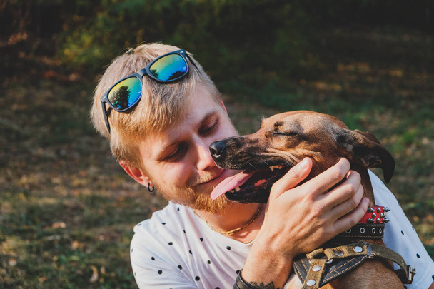 Human and dog friendship: young man hugs his dog outdoors - Photo, image
