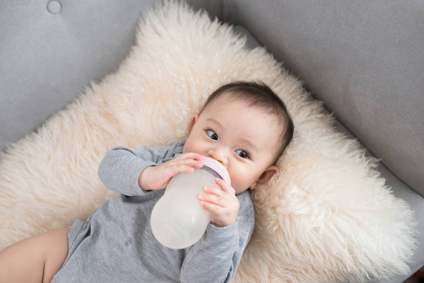 Азиатский младенец ест молоко из бутылки, через 9 месяцев после рождения
 - Фото, изображение