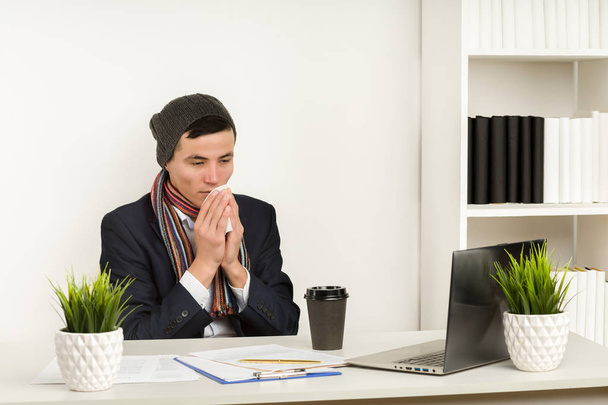 若いアジアのビジネスマンは、オフィスでラップトップで作業しながら、彼の鼻を吹く. - 写真・画像
