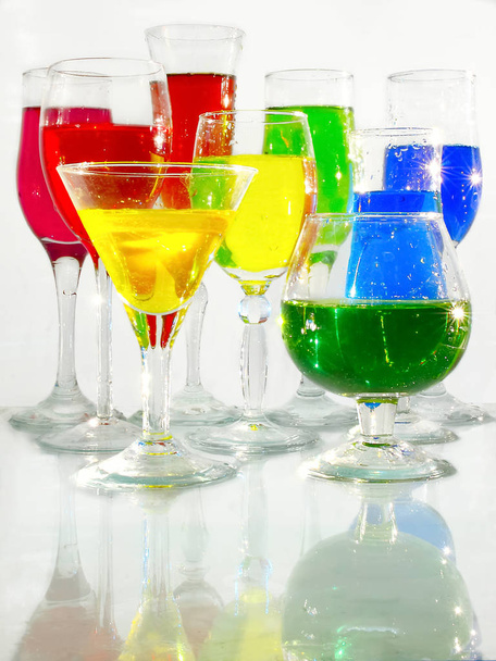 Vinné brýle s červenými, modrými, zelenými, žlutými kapalinami stojí na skleněném povrchu na bílém pozadí - Fotografie, Obrázek