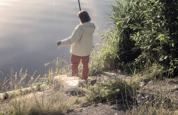 Γυναίκα που ψαρεύει στην ακτή μιας όμορφης λίμνης. - Φωτογραφία, εικόνα