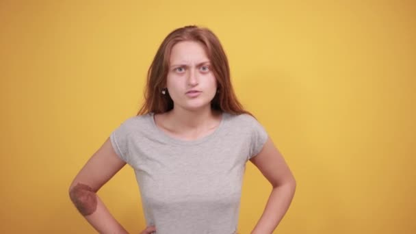 brunette meisje in grijs t-shirt over geïsoleerde oranje achtergrond toont emoties - Video