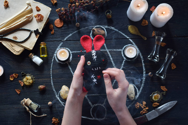 In Voodoo konijn zijn naalden pricked. Kaarsen, Pentagram, stenen, liefde potion en oude boeken op heks tafel. Occulte, esoterische of waarzeggerij concept. Mystic, Halloween en vintage achtergrond - Foto, afbeelding