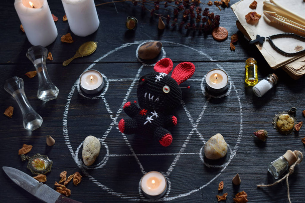 Im Voodoo-Kaninchen werden Nadeln gestochen. Kerzen, Pentagramm, Steine, Liebestrank und alte Bücher auf dem Hexentisch. okkultes, esoterisches oder weissagerisches Konzept. Mystischer, halloween und vintage Hintergrund - Foto, Bild