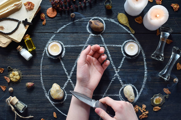 Womens hands and knife on pentagram circle with candles, stones, love potion and old books on witch table. Occult, esoteric or divination concept. Mystic, Halloween and vintage background - Foto, Imagem