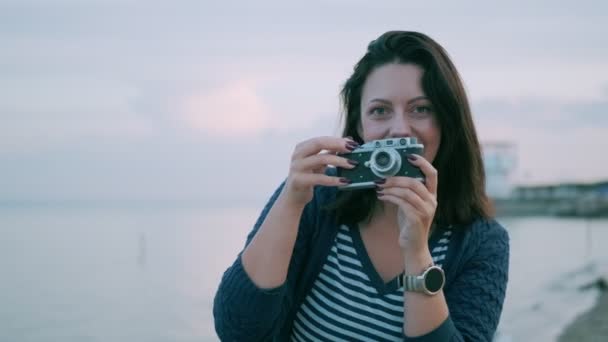 Młoda kobieta robi zdjęcia na Vintage kamery nad oceanem. portret dziewczyny z kamerą retro - Materiał filmowy, wideo