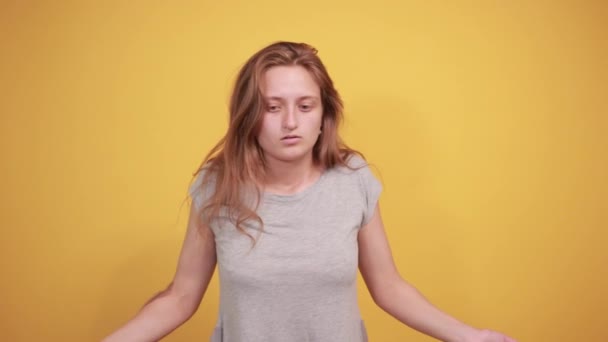 brunetka v šedém tričku nad ojedinělým oranžovým pozadím vykazuje emoce - Záběry, video