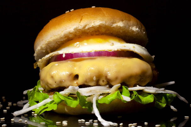 ζουμερό burger με αυγό, μοσχαρίσια μπριζόλα, τυρί και μαρούλι σε σκούρο φόντο - Φωτογραφία, εικόνα