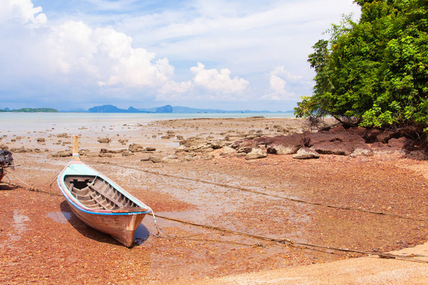 Traditional longtail boat on the sand beach at the low tide. Sea view with islands on horizon and clouds in the sky. - 写真・画像