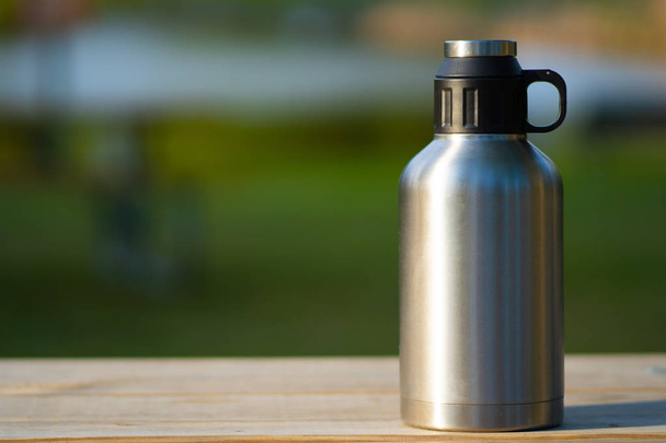Closeup of large thermos on a wooden table outside on a green bl - Foto, Imagem