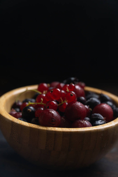 Ripe black and red currants in a wooden bowl on a wooden table. Organic food, berries, harvest season. - Fotoğraf, Görsel