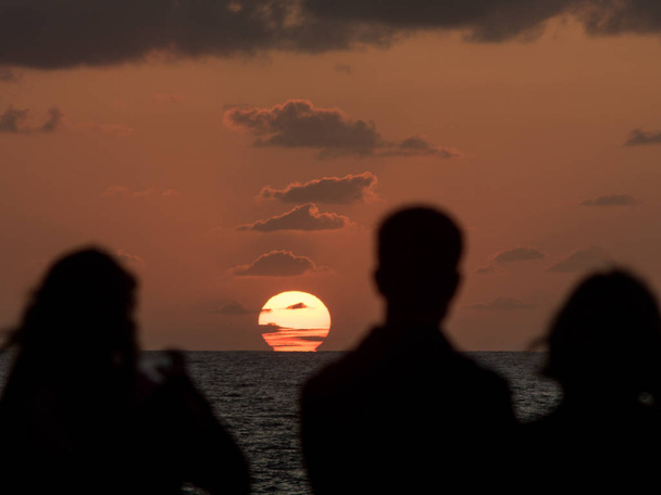 Des silhouettes de gens regardant le coucher du soleil près de l'océan
 - Photo, image