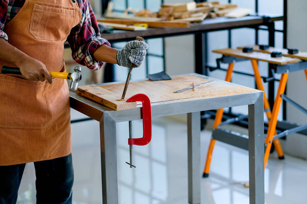 Viejo artesano utiliza martillo y cincel para trabajar con madera y producir algún producto en su lugar de trabajo durante el día
. - Foto, Imagen