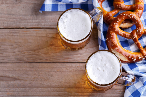 Two pints of beer and pretzels on a blue table cloth, Octoberfest snack - Фото, изображение