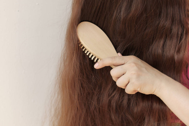 girl with long hair combing them with a wooden comb, horizontal, close-up - Photo, Image