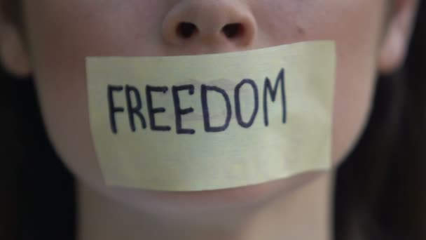 Freedom written on tape, woman removing mouth sticker, rights oppression, block - Кадры, видео