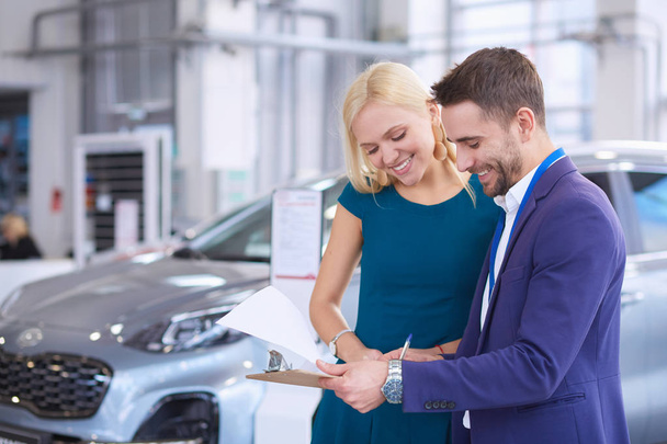 Car salesman sells a car to happy customer in car dealership and hands over the keys - Foto, Imagen