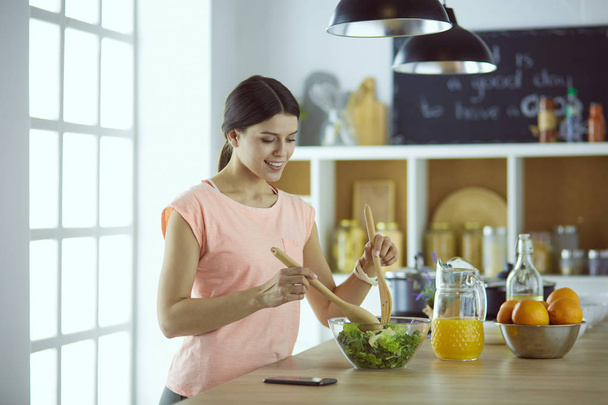 Smiling young woman mixing fresh salad in the kitchen. - Photo, image