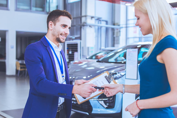 Car salesman sells a car to happy customer in car dealership and hands over the keys - 写真・画像