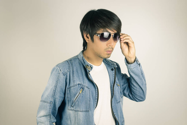 junger asiatischer Mann in Jeans oder Jeansjacke berührt Sonnenbrille in  - Foto, Bild