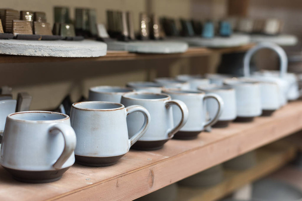 glazed ceramic dishes stand on a shelf in the workshop shelving with handmade ceramic and clay mugs - Foto, imagen