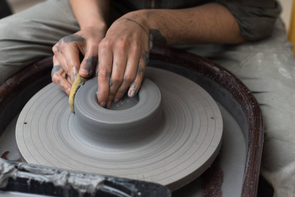 Auf einer Töpferscheibe stellt der Meister Produkte aus grauem Ton her. Mädchen schafft eine Keramikvase - Foto, Bild