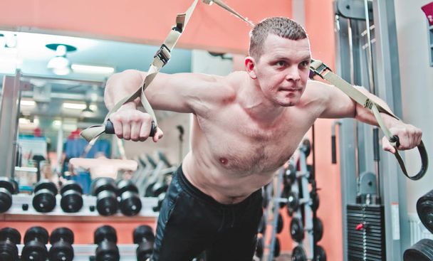 Fuerte hombre hace crossfit flexiones con correas de fitness en el gimnasio  - Foto, Imagen