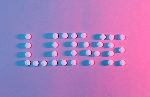 Inscription love with pills. The concept of dependence. Many white pills, red-blue neon light. - Foto, imagen