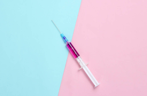 Minimalism medical concept, injection, vaccination. Syringe with purple liquid on blue pink pastel background. - Фото, изображение