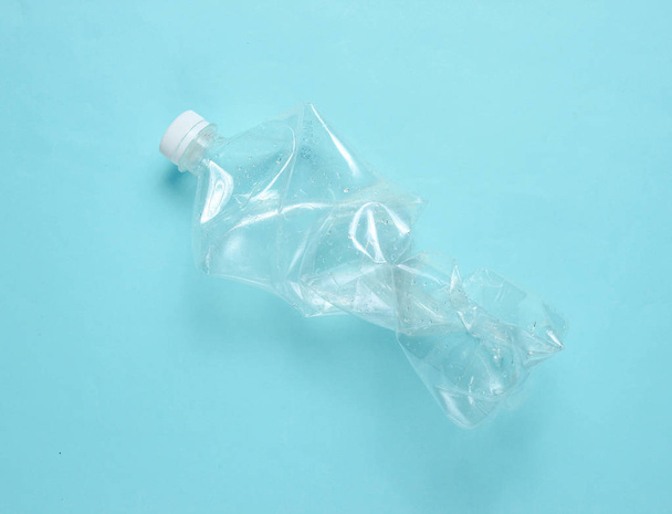 Minimalistic ecological concept. Crumpled plastic bottle on blue background. Environmental plastic pollution - Фото, зображення