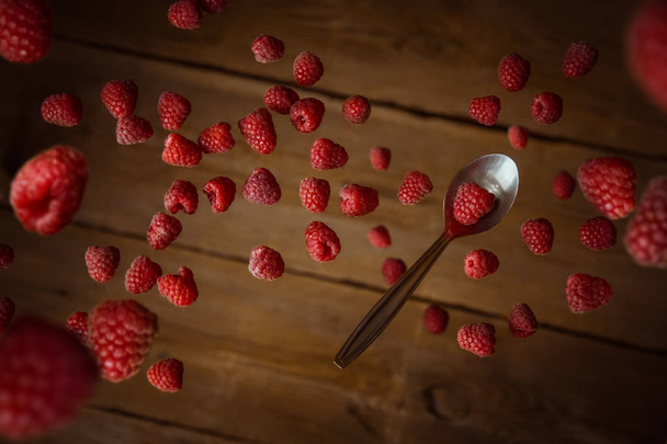 red raspberries with a teaspoon in flight fall on a wooden rustic table top view - Foto, afbeelding
