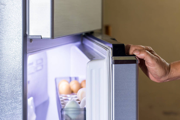 Αφηρημένο θηλυκό χέρι της γυναίκας ανοίγει ένα γκρι ψυγείο Ντου - Φωτογραφία, εικόνα