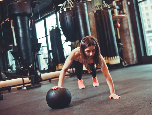 Žena dělá kliky whith medicína míč v tmavé tělocvičně - Fotografie, Obrázek