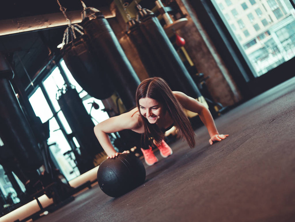 Woman doing push ups whith medicine ball  at dark gym - Φωτογραφία, εικόνα