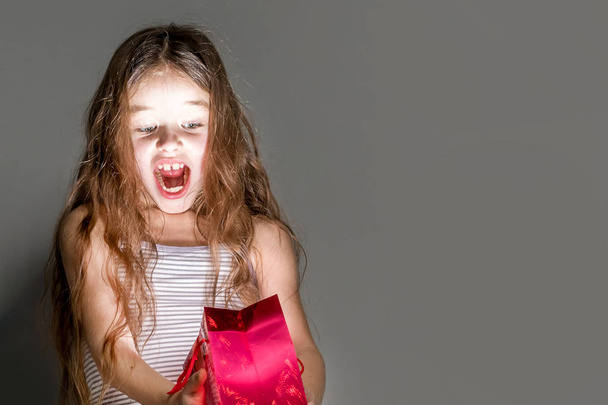Scared girl looks in a red glowing gift bag on a gray background - Фото, зображення