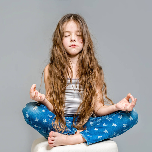 Little girl meditating in the lotus position on a gray backgroun - Foto, imagen