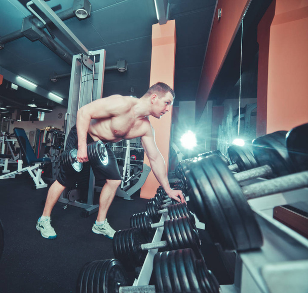 Young handsome adult male doing one-arm dumbbell rows in modern gym - Фото, зображення